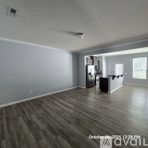 A room with wooden flooring and a kitchen area in the background.