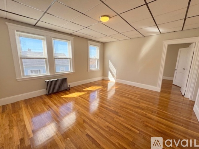 A room with wooden floors and white walls has a window and a radiator.