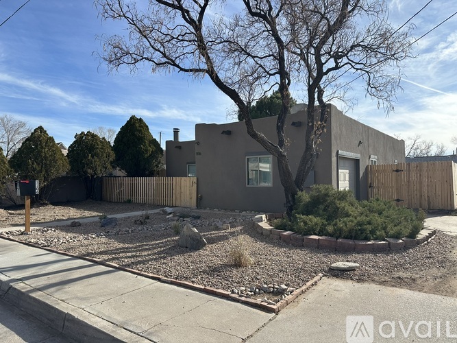 A house with a grey exterior is surrounded by a gravel area and a small tree.