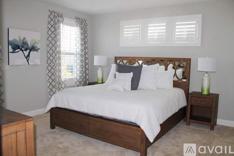 A bedroom with a large bed, two lamps, and a painting on the wall.