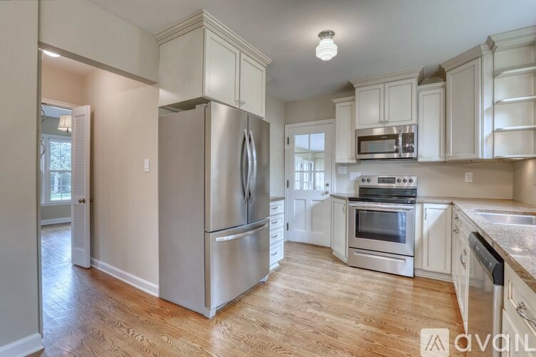 A stainless steel refrigerator stands in a kitchen with wooden floors and white cabinets.