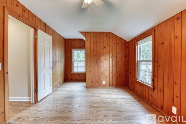 A room with wooden walls and floors, a ceiling fan, and a window.