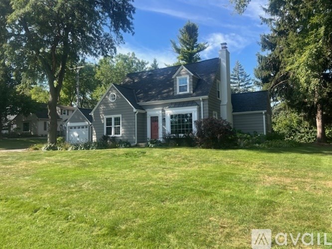 A house with a grey roof and a red door is surrounded by green grass and trees.