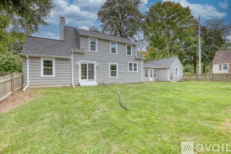 A house with a grey exterior and a white door is surrounded by a green lawn.
