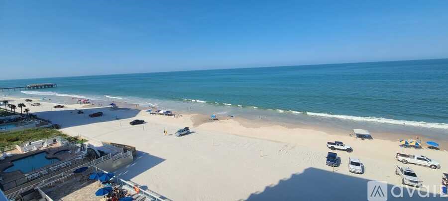 A beach with a parking lot and a pier in the distance.