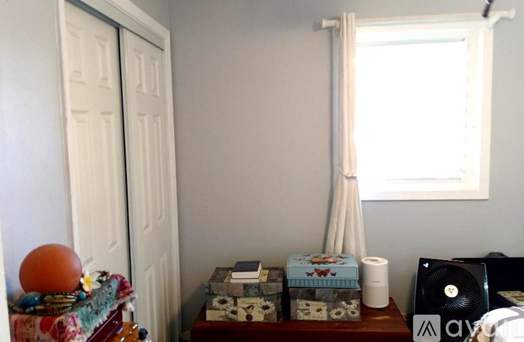 A room with a white door, a window with white curtains, and a table with various objects on it.