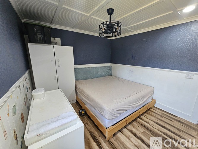 A small bedroom with a bed, a fridge, and a wooden floor.