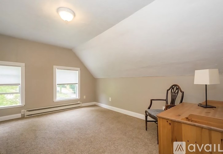 A room with a window, a chair, and a table with a lamp on it.