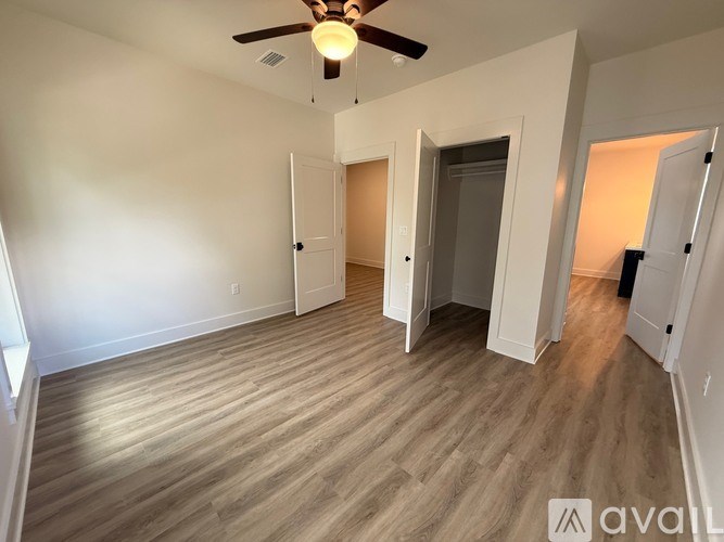 A room with a ceiling fan and light, hardwood floors, and white walls with a door to the right.