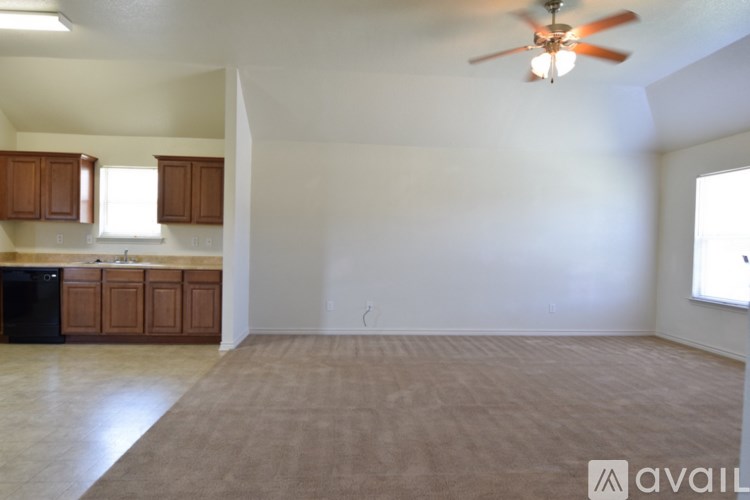 A room with a ceiling fan and a kitchen area with wooden cabinets and a black dishwasher.