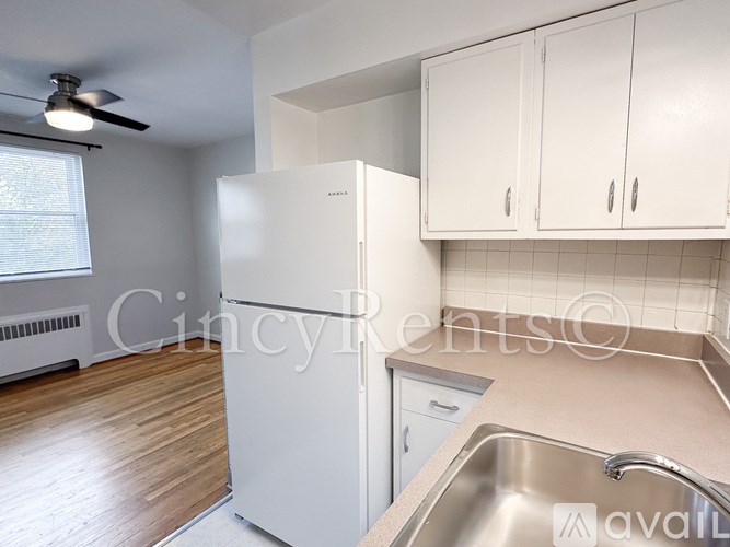 A kitchen with a white fridge, wooden floors, and white cabinets.