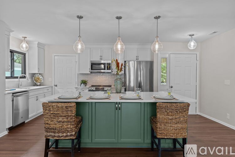 A kitchen with a green island and two wicker chairs.