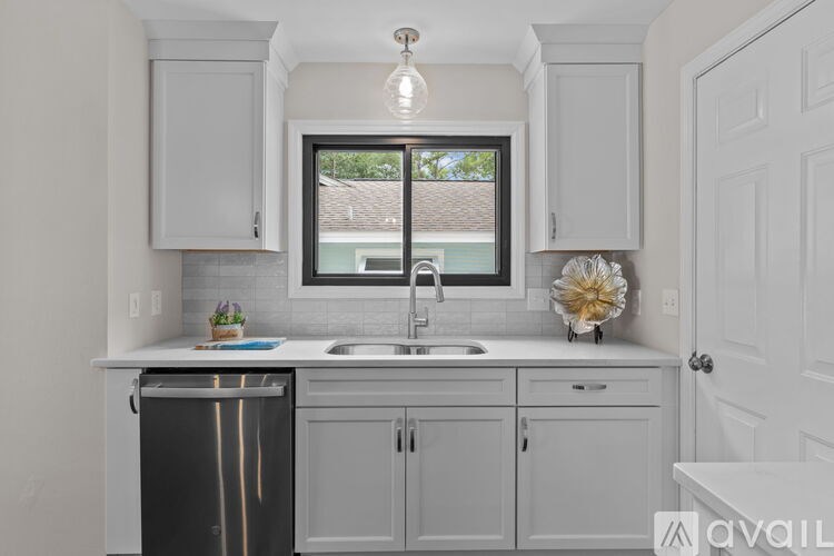 A kitchen with white cabinets and a window overlooking a roof.