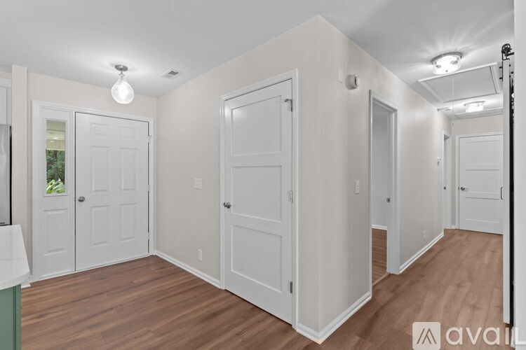 A room with white walls and wooden floors, with a white door on the left and a white closet on the right.