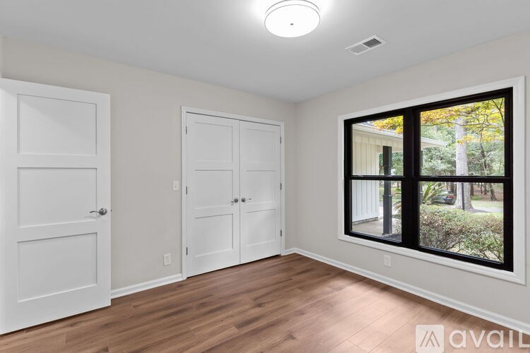 A room with a large window, hardwood floors, and white walls with two doors.