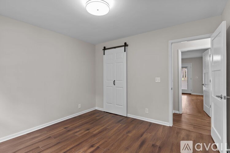 A room with wooden floors and white walls, a door, and a mirror.