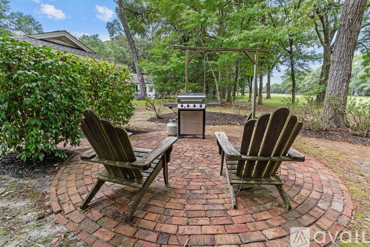 Two chairs are on a brick patio with a grill in the middle.