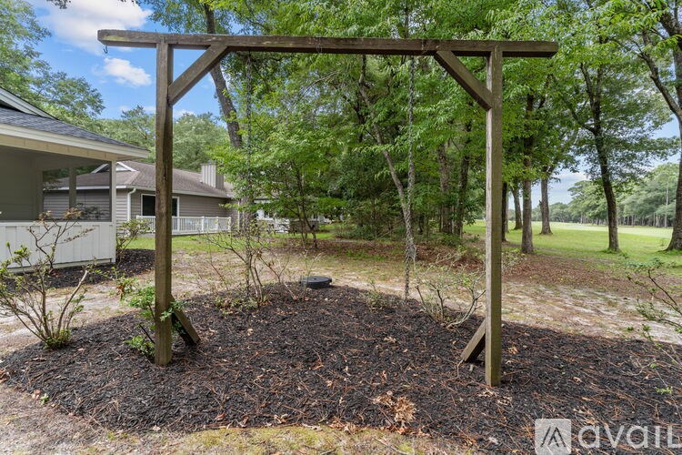 A wooden pergola stands over a mulched garden bed.