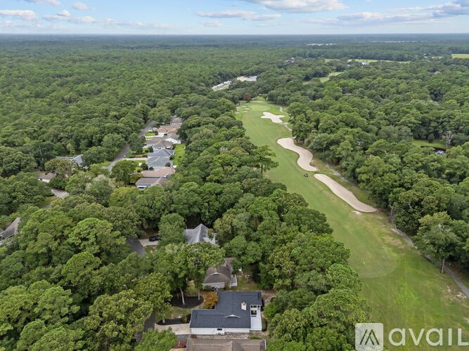 A bird's eye view of a lush green forest with a winding path and a few buildings.