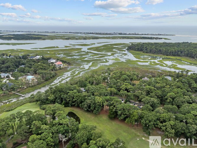 A bird's eye view of a lush green landscape with a body of water and a few buildings.