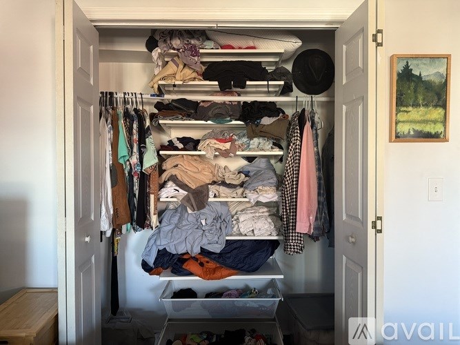 A small closet is packed with clothes and other items.