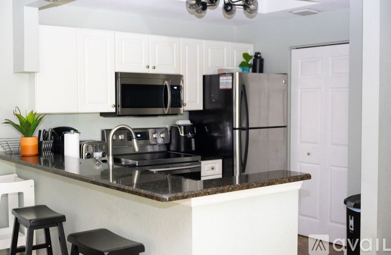 A kitchen with a black fridge and microwave, a white counter, and a white cabinet.