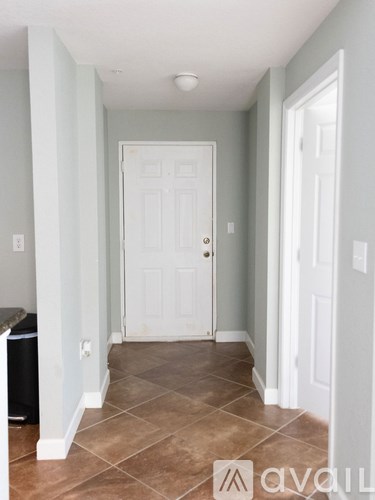 A hallway with a white door and brown tile flooring.
