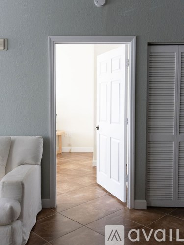 A white chair is in the corner of a room with a door open to another room.