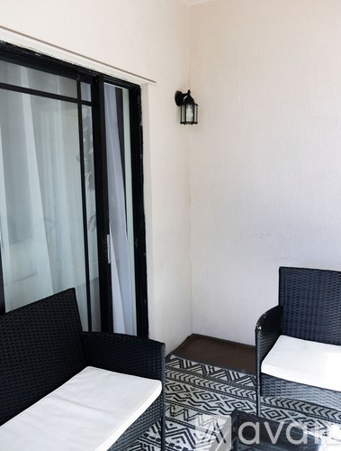 A black and white patterned bed sits next to a window with sheer curtains.