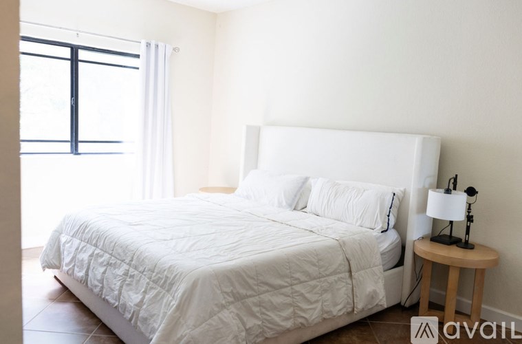 A white bed with a white headboard and a white bedspread is in a room with a window.