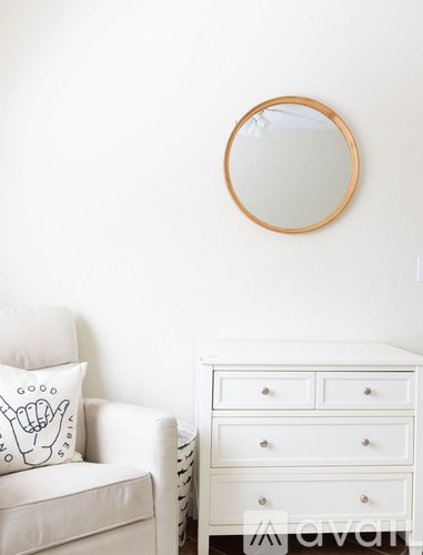 A white couch with a pillow and a mirror above it.