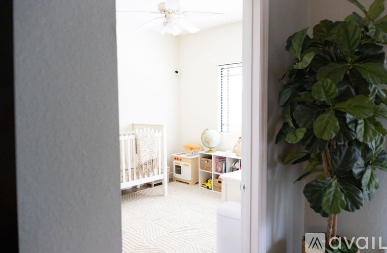 A baby crib sits in a room with a fan and a plant.