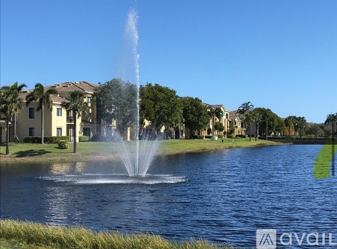 A fountain in the middle of a lake with houses in the background.