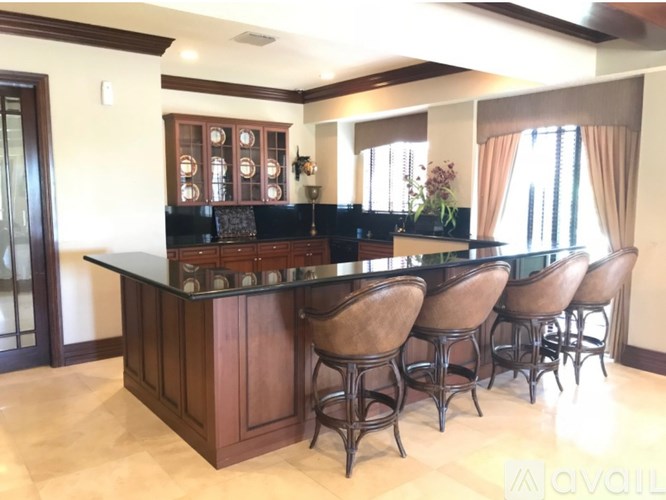 A bar with stools is in a room with wooden cabinets and a counter.