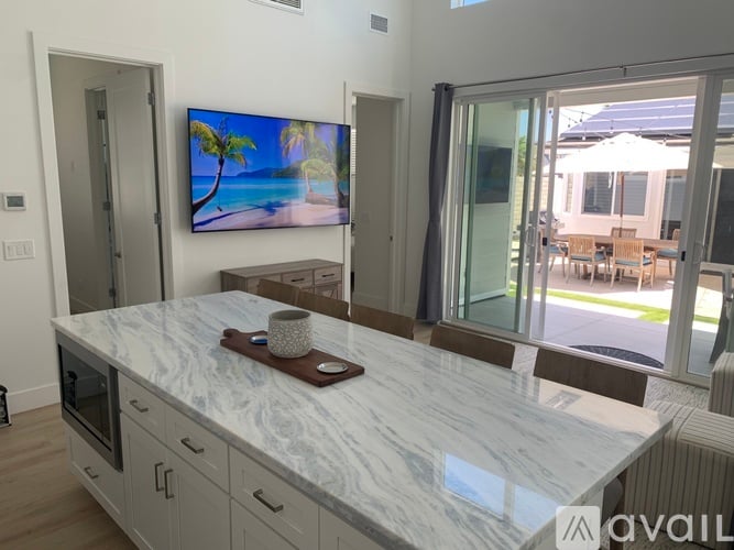 A modern kitchen with a marble countertop and a television displaying a beach scene.