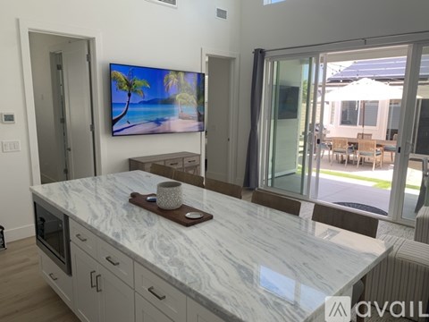 A modern kitchen with a marble countertop and a television displaying a beach scene.