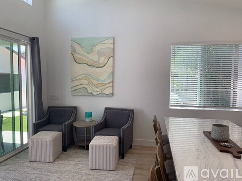 A living room with a grey sofa, ottoman, and a painting on the wall.