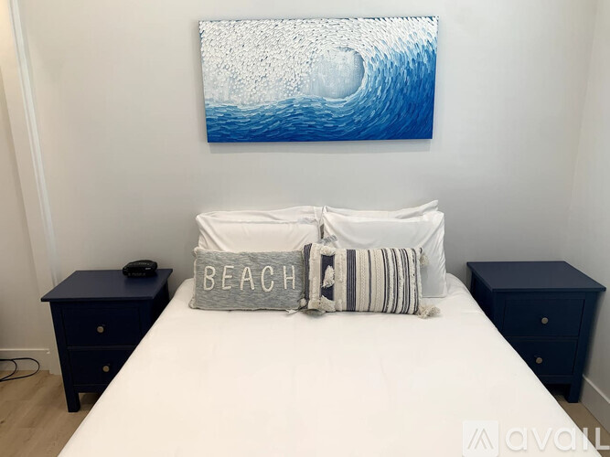 A bedroom with a white bed, a blue painting, and two navy blue nightstands.