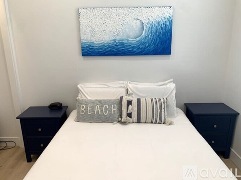 A bedroom with a white bed, a blue painting, and two navy blue nightstands.