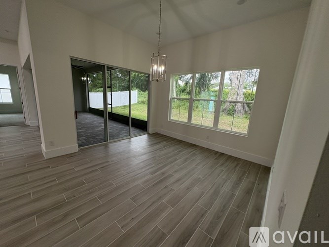 A spacious room with wooden flooring and large windows overlooking a green area.