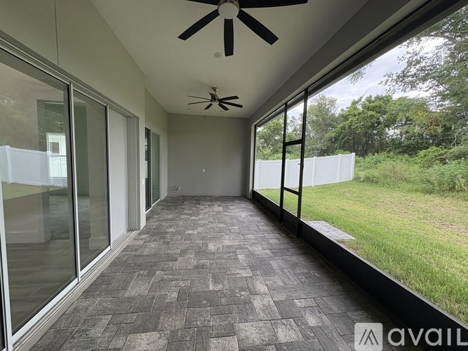A room with a ceiling fan and large windows overlooking a grassy area.