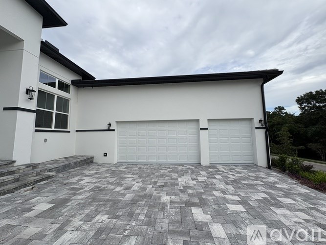 A white house with a black roof and two garage doors.