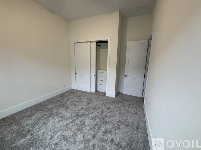 A room with grey carpet and white walls, featuring a white wardrobe with a mirror and a white door.