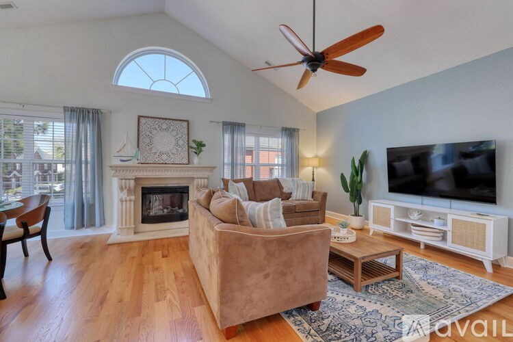 A living room with a beige couch, a fireplace, a ceiling fan, and a television.
