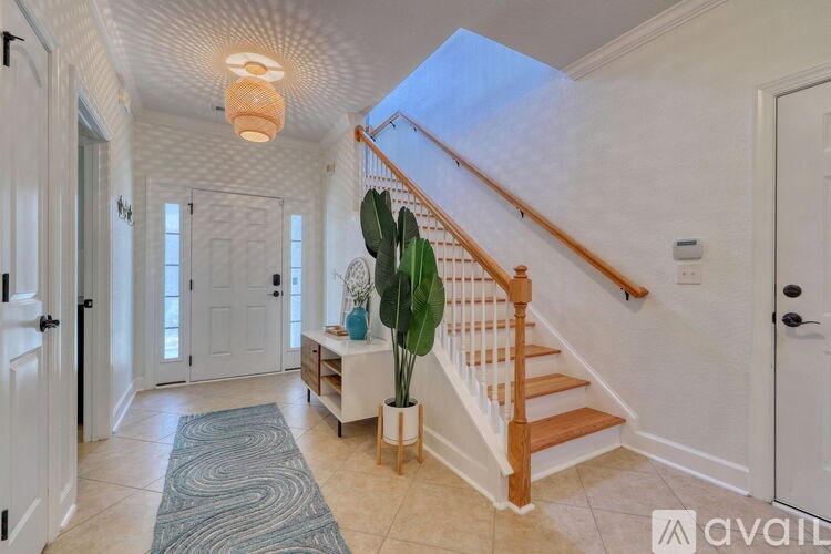A hallway with a staircase, a potted plant, and a rug.