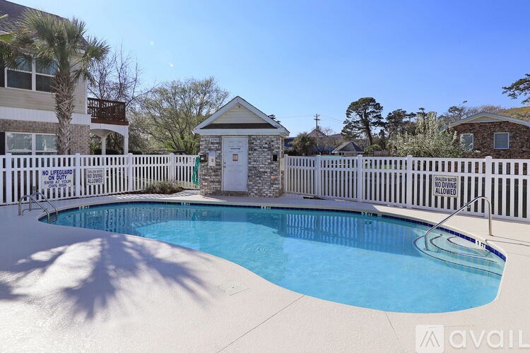 A pool surrounded by a white fence with a small building in the background.