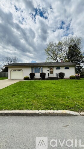 A house with a white exterior and a grey roof is surrounded by a green lawn.