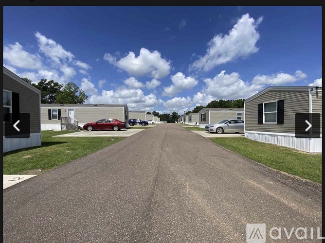 A street view of a residential area with houses on both sides and cars parked in the distance.