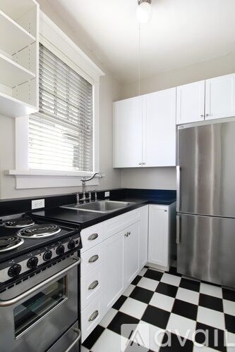 A black and white checkered floor in a kitchen with white cabinets and a stainless steel refrigerator.