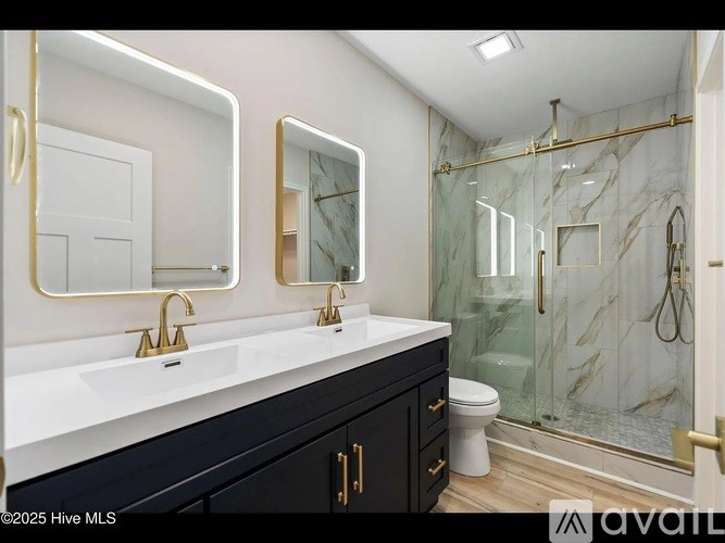 A bathroom with a marble shower and gold fixtures.